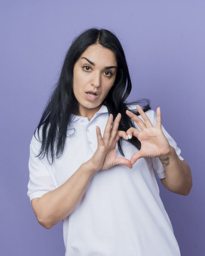 confianza joven morena caucasica gestos corazon signo de mano aislado en la pared purpura